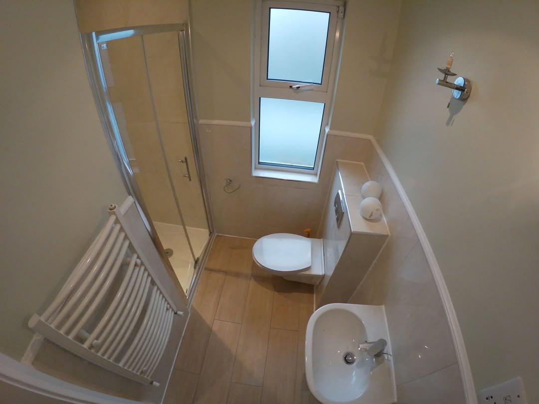 Small bathroom with shower, toilet, sink, and heated towel rack.