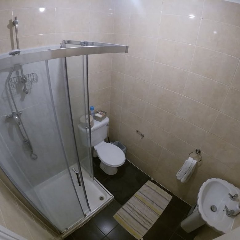 Small bathroom with shower, toilet, and sink. Neutral tile and black floor.