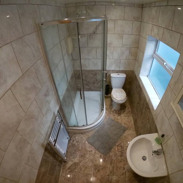 Small bathroom with shower, toilet, sink, tiled walls and floor, window, and heated towel rack.