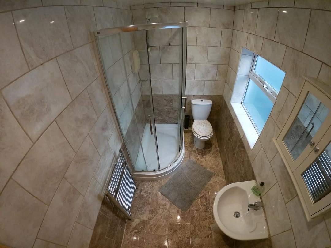 Small bathroom with shower, toilet, sink, tiled walls and floor, window, and heated towel rack.
