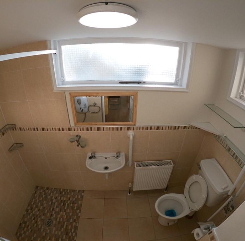 Small bathroom with shower, toilet, sink, and window. Neutral tile.
