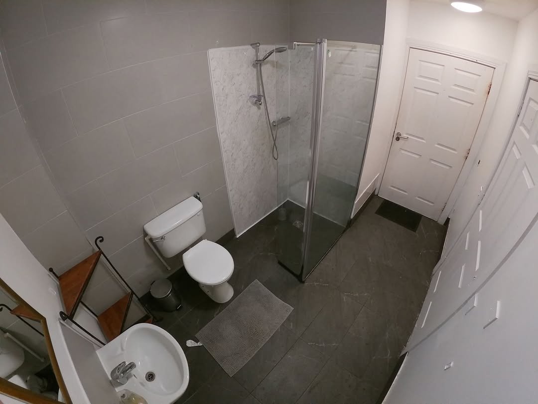 Small bathroom with shower, toilet, sink, and gray tile flooring.
