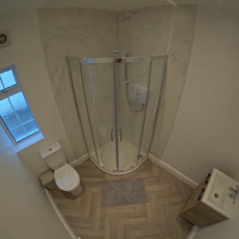 Small bathroom with shower, toilet, and sink. Herringbone floor.