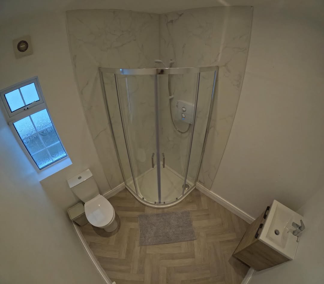 Small bathroom with shower, toilet, and sink. Herringbone floor.