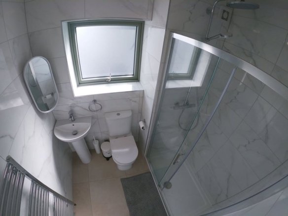 Small bathroom with shower, toilet, sink, heated towel rack, and window. White marble tile walls.