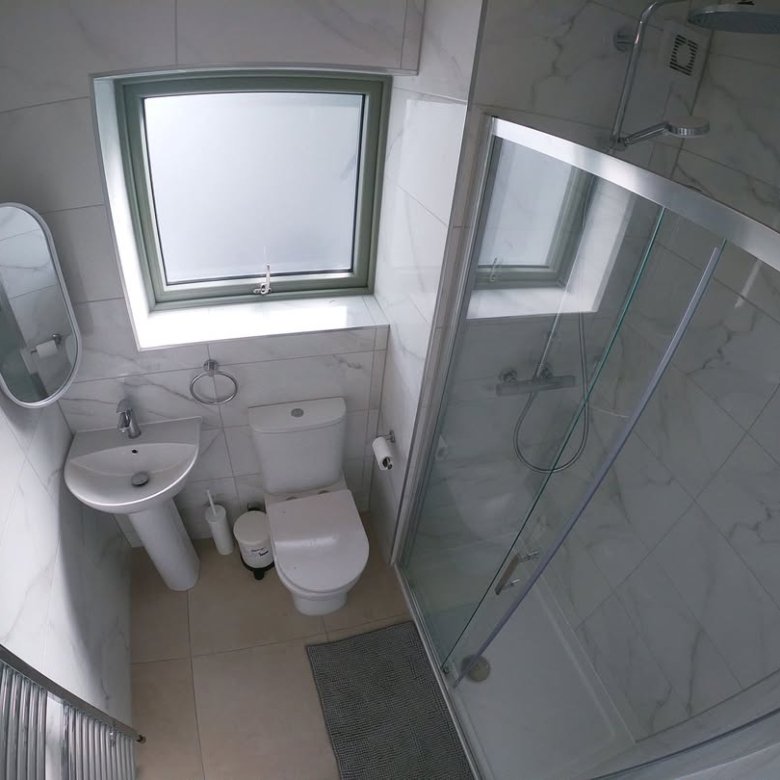 Small bathroom with shower, toilet, sink, heated towel rack, and window. White marble tile walls.