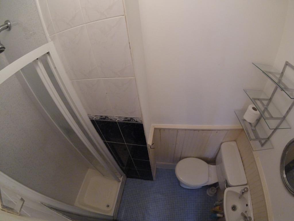 Small bathroom with shower, toilet, sink, and glass shelves.