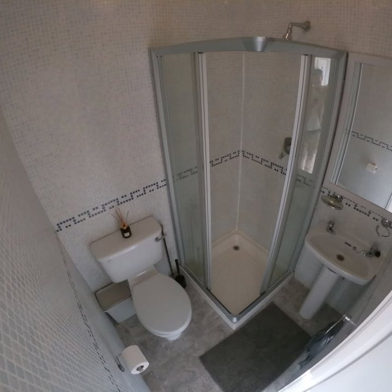 Small bathroom with shower, toilet, and sink. White mosaic tiles.