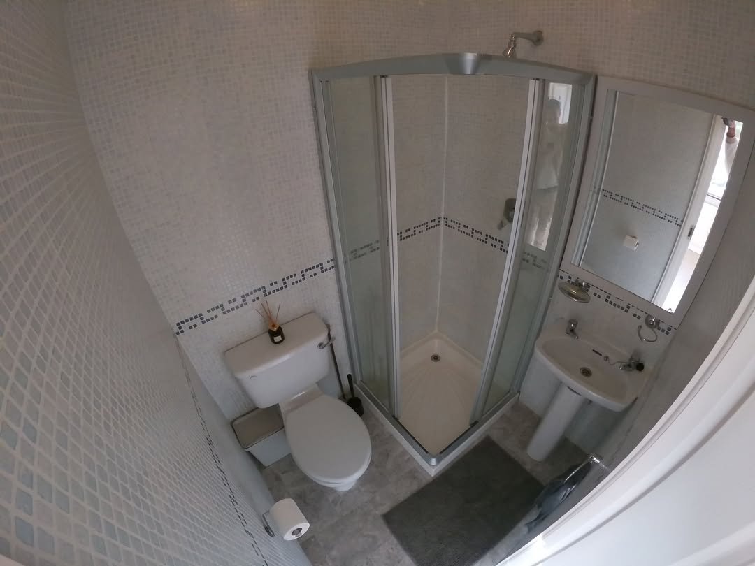 Small bathroom with shower, toilet, and sink. White mosaic tiles.