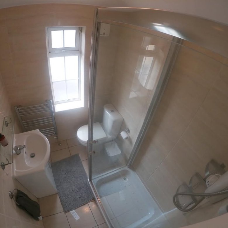 Small bathroom with shower, toilet, sink, and window. Neutral tile walls and gray rug.