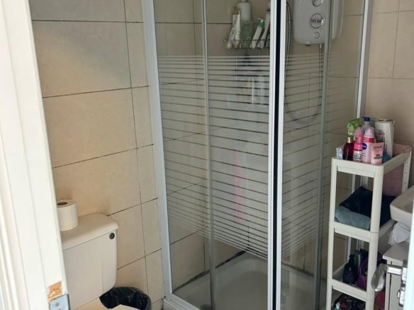 Small bathroom with shower, toilet, and storage shelves; beige tiles.