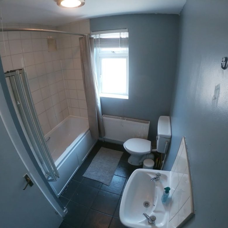 Bathroom with toilet, sink, bathtub, shower curtain, and window.