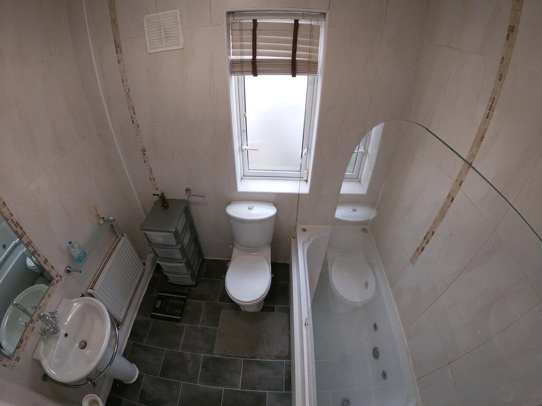 Small bathroom interior with toilet, sink, bathtub, and window.