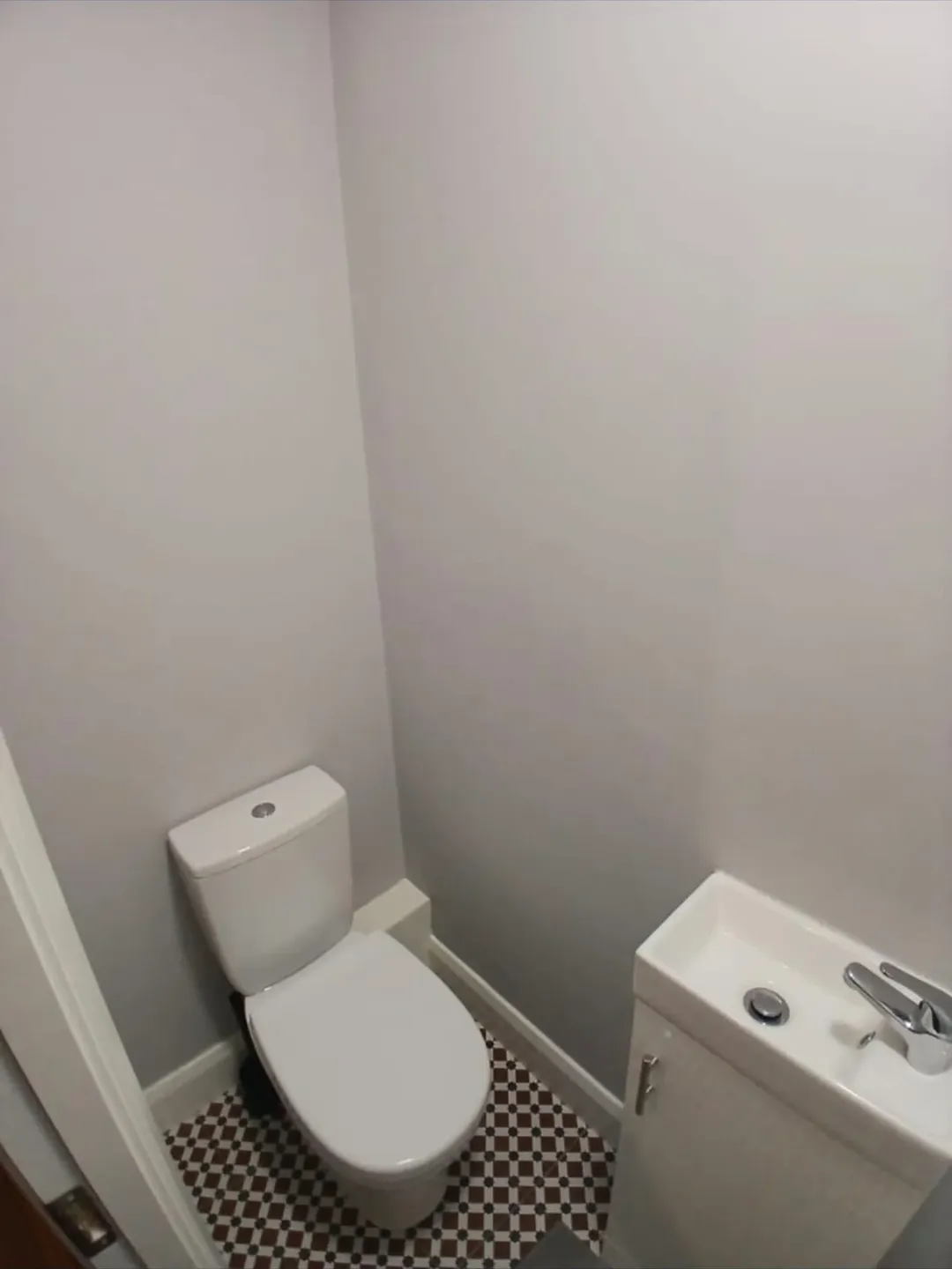 Small bathroom with toilet and sink against gray walls, patterned floor.