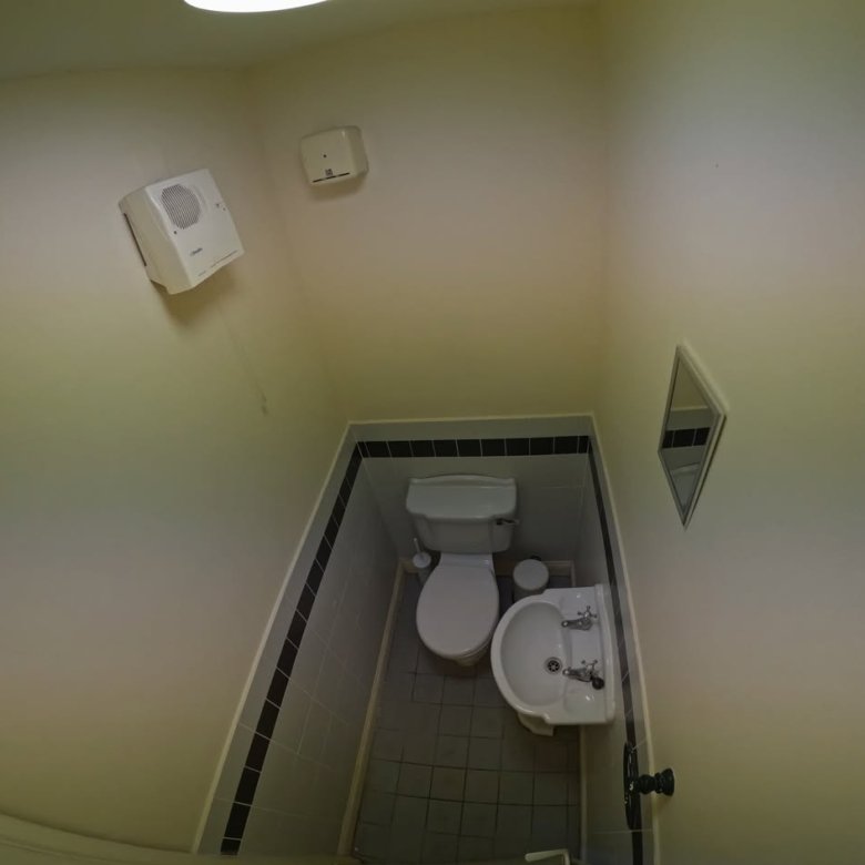 Small bathroom with toilet, sink, and mirror. White walls with black trim.