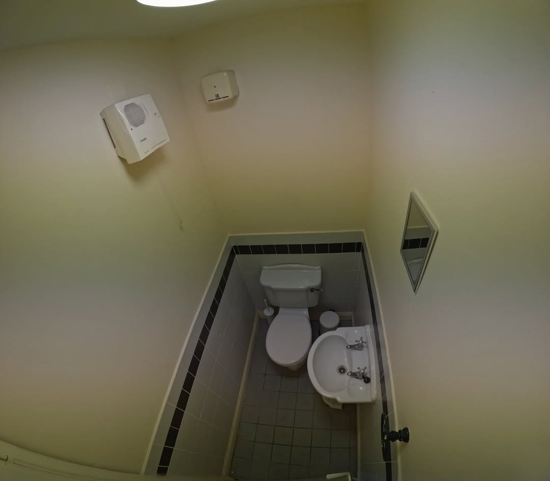 Small bathroom with toilet, sink, and mirror. White walls with black trim.