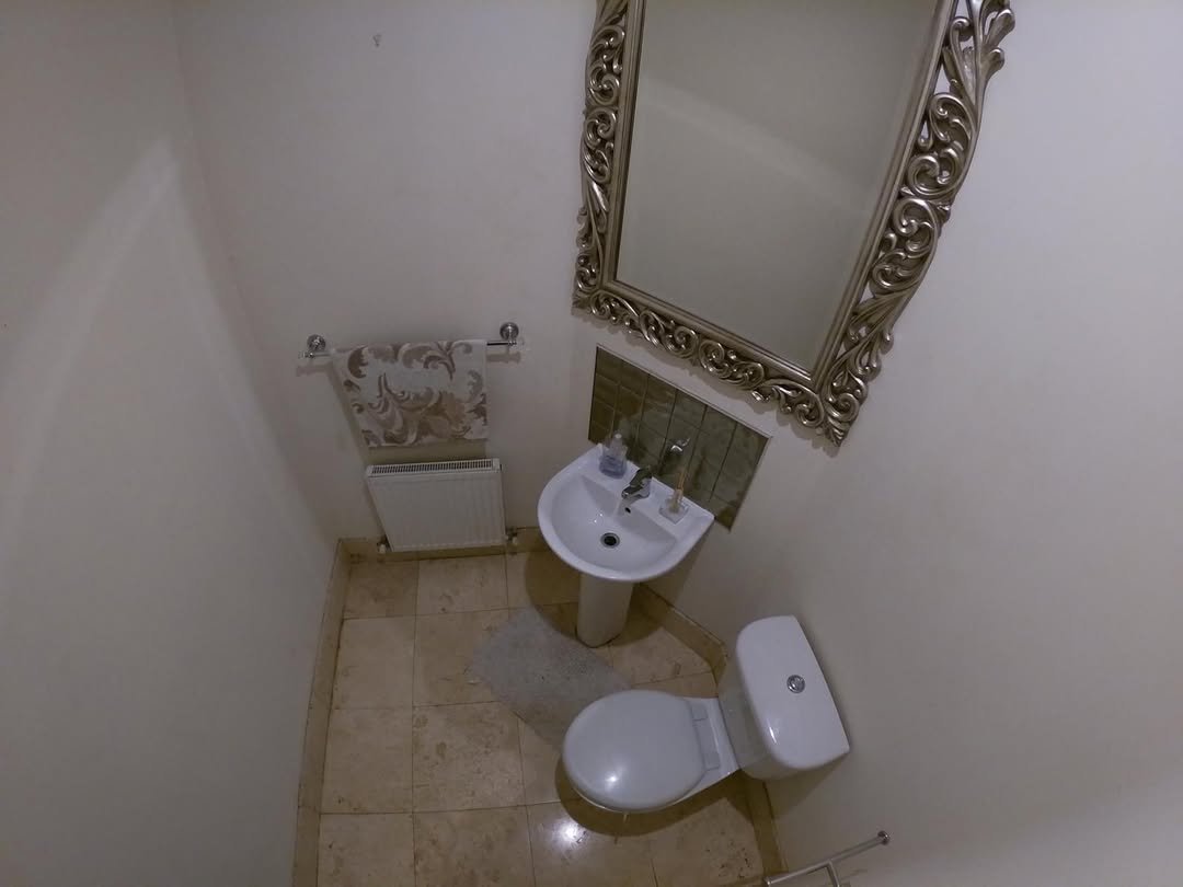 Small bathroom with toilet, sink, decorative mirror, and beige tile floor.
