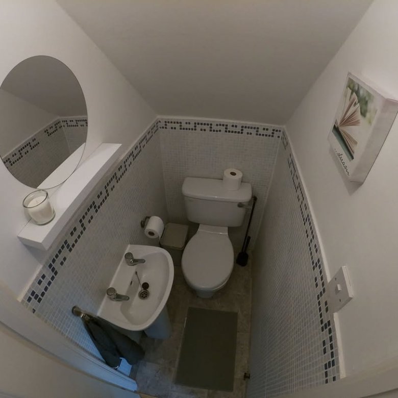 Small bathroom with toilet, sink, round mirror, and mosaic tile border.