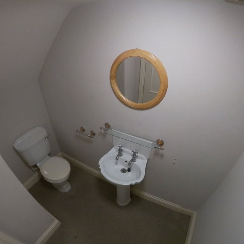 Small bathroom with toilet, sink, round mirror, and coat hooks on white wall.