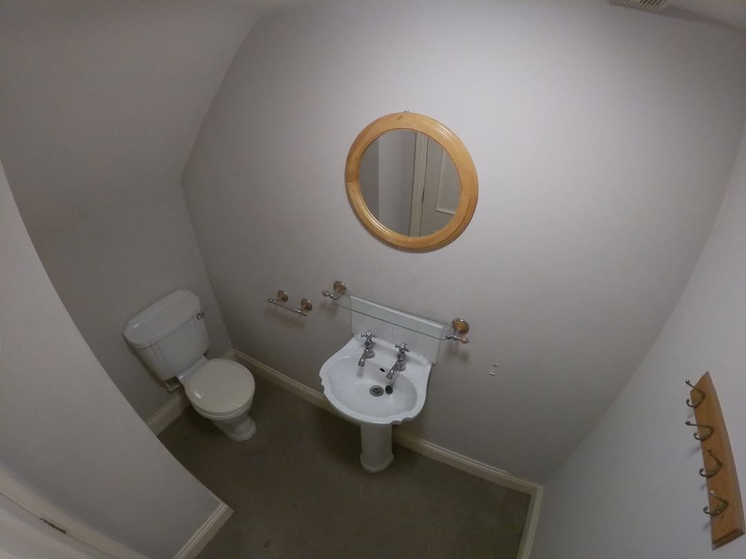 Small bathroom with toilet, sink, round mirror, and coat hooks on white wall.