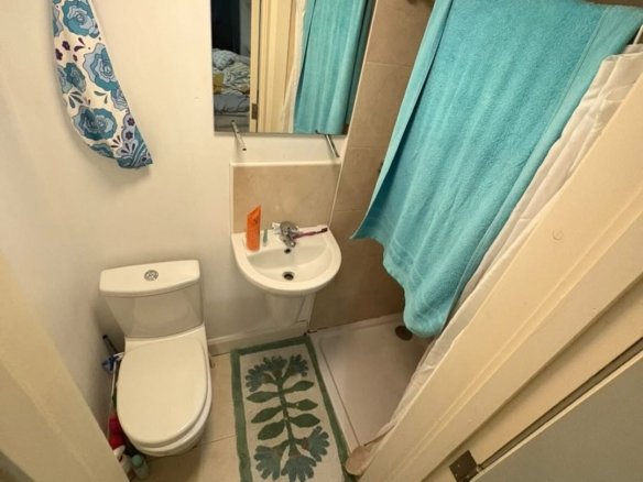 Small bathroom with toilet, sink, shower, and blue towels.