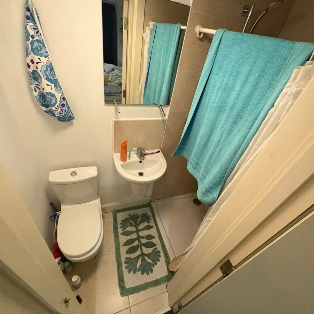 Small bathroom with toilet, sink, shower, and blue towels.