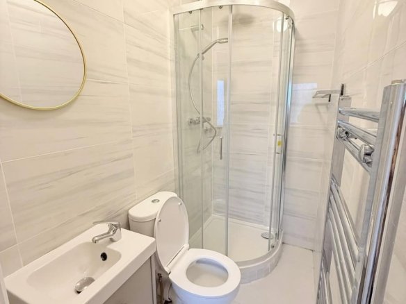 Small bathroom with toilet, sink, shower, and towel warmer. Neutral tile and modern fixtures.