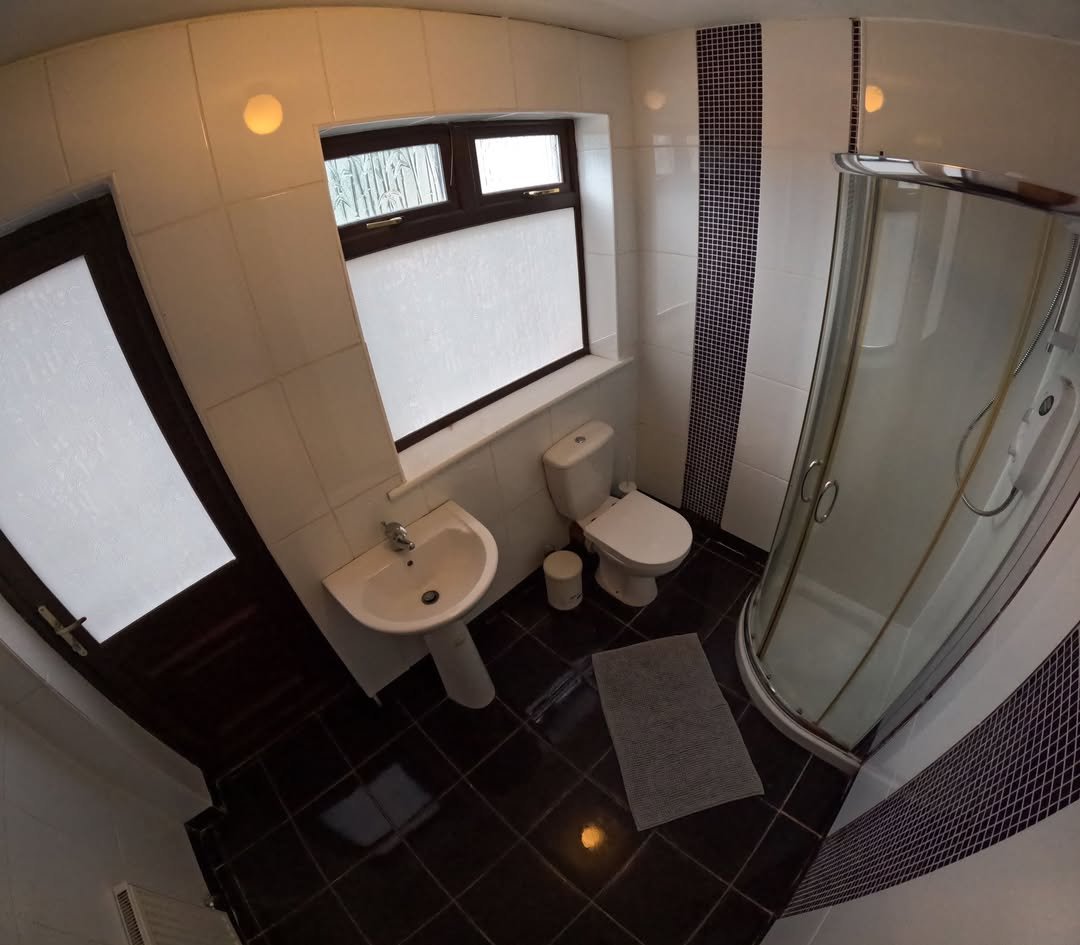 Small bathroom with toilet, sink, and shower stall, dark tile floor.