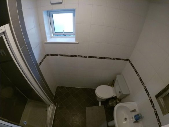 Compact bathroom featuring a toilet, sink, and glass-enclosed shower stall with dark tile flooring.