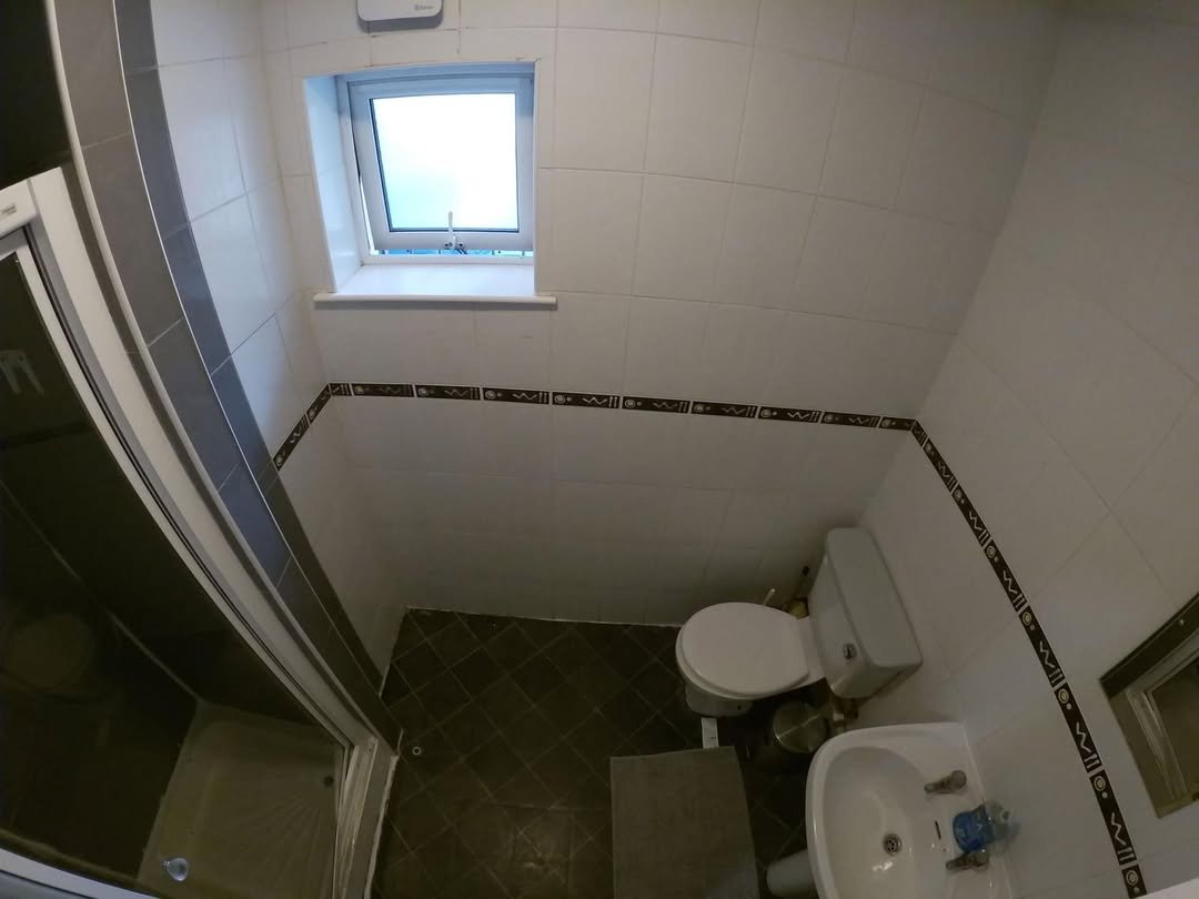 Compact bathroom featuring a toilet, sink, and glass-enclosed shower stall with dark tile flooring.