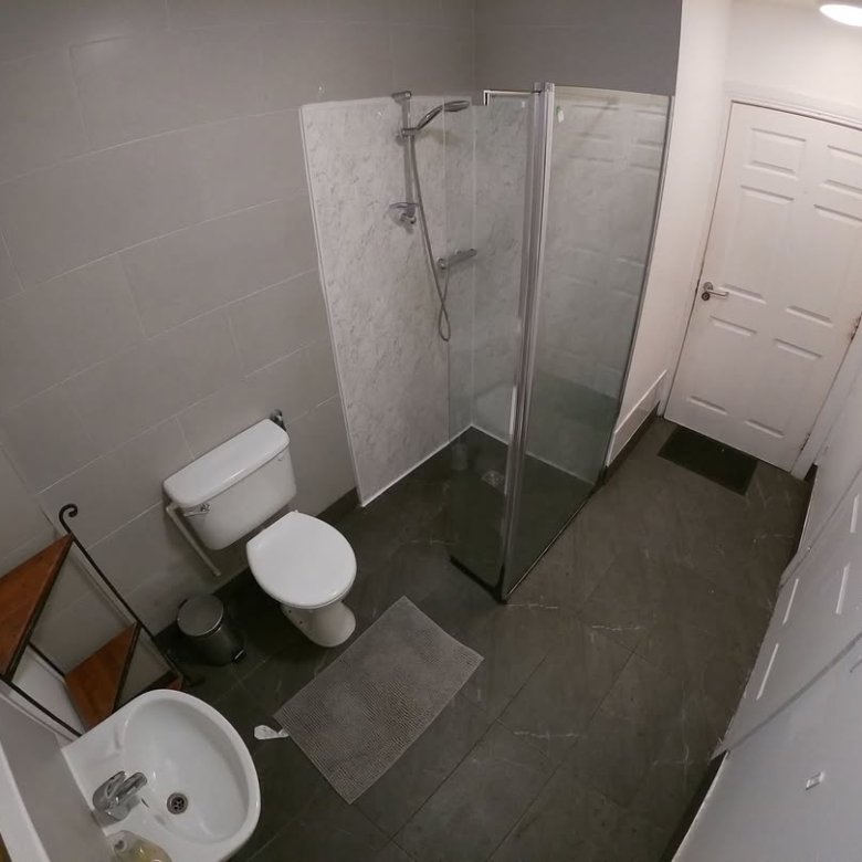 Small bathroom with toilet, sink, and shower enclosure. Gray tile floor and walls.
