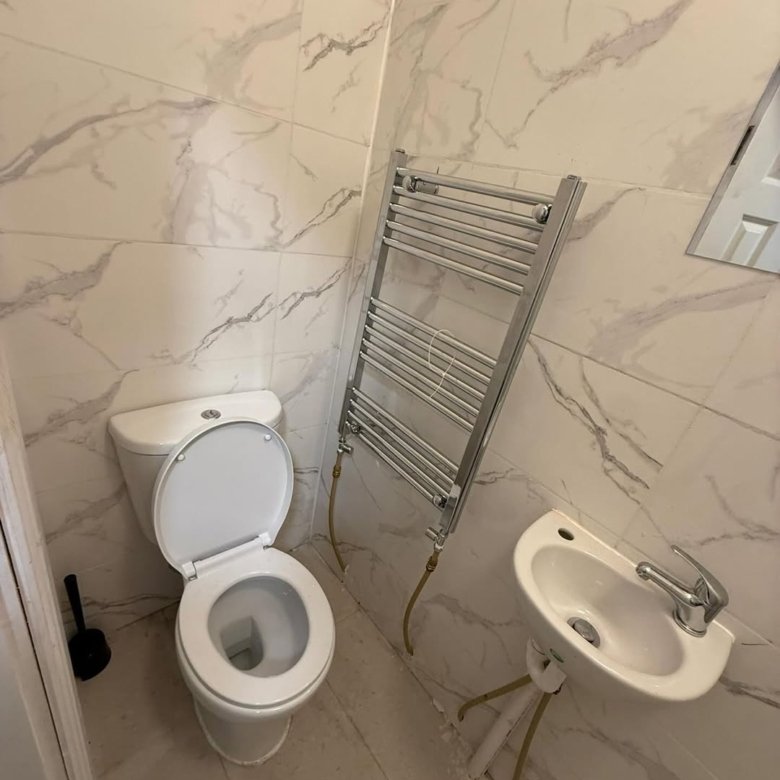 Small bathroom with toilet, sink, and towel rack against marble walls.