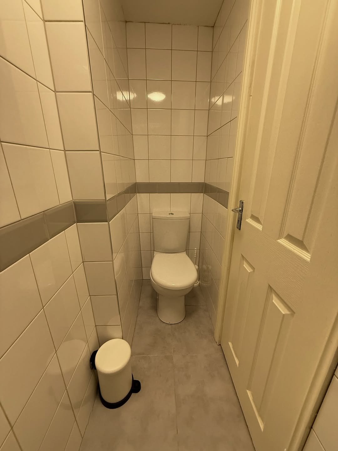 Small bathroom with toilet, tiled walls, and a white door.