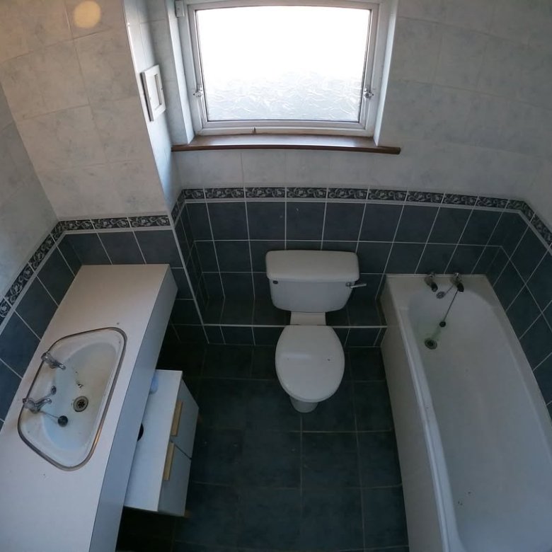 Compact bathroom with toilet, tub, sink, and blue tile. Skylight provides natural light.