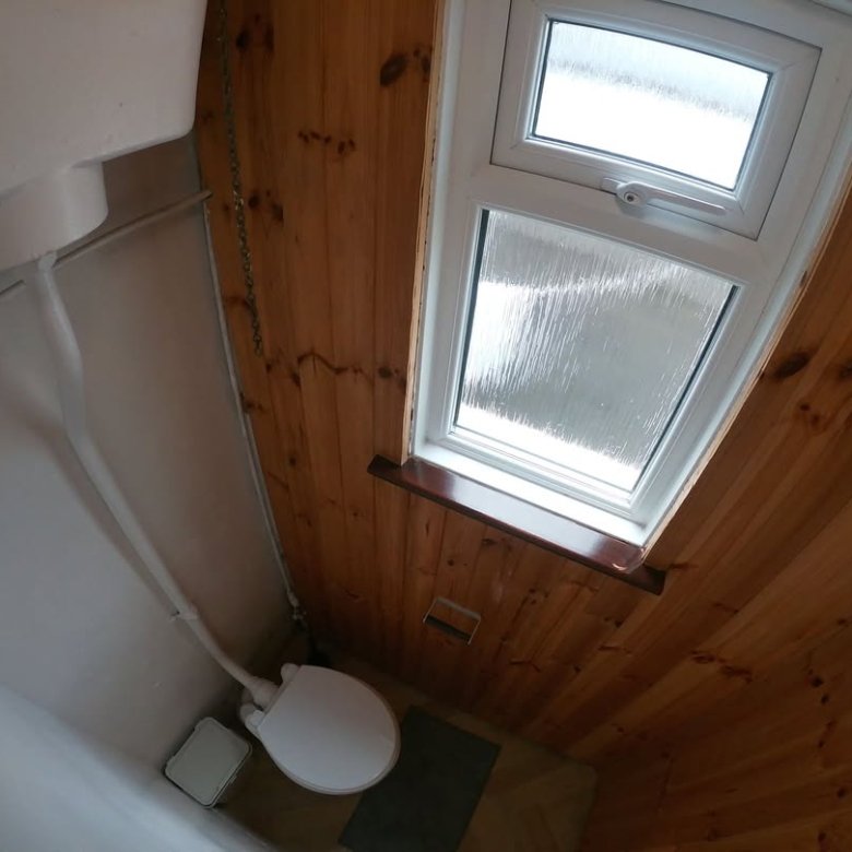 Small bathroom with toilet, wood paneling, and window. Overhead view.