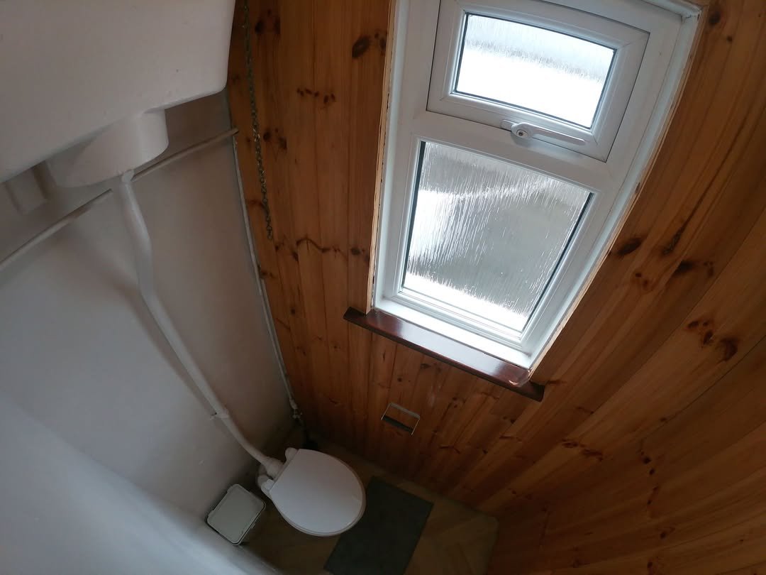 Small bathroom with toilet, wood paneling, and window. Overhead view.