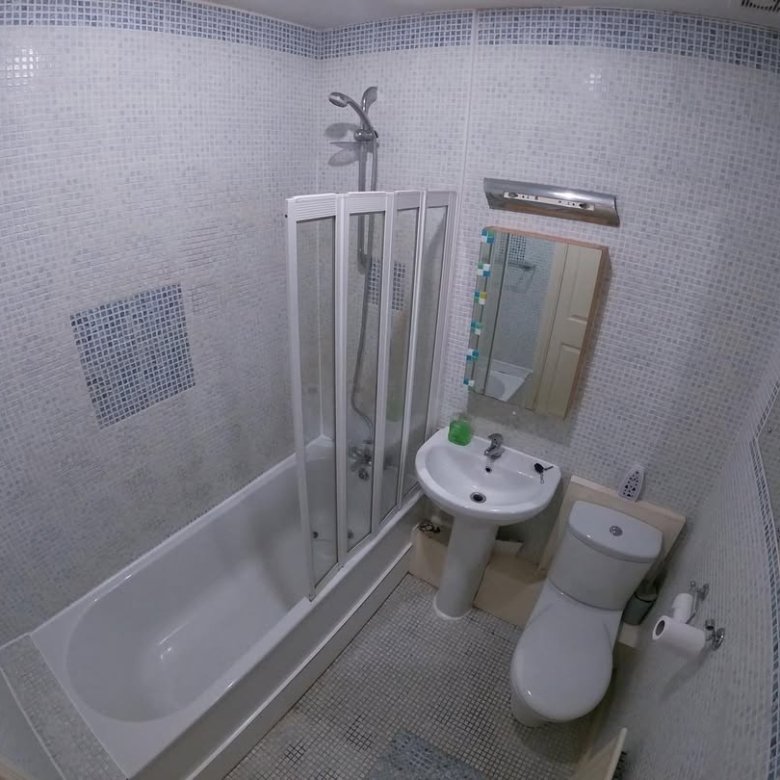 Small bathroom with tub, shower, toilet, and sink. Mosaic tile walls.