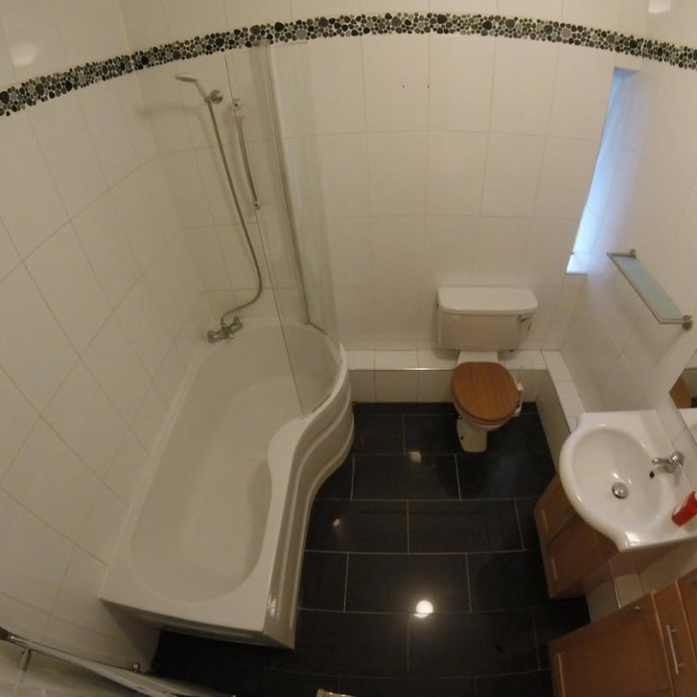 Small bathroom with tub, toilet, sink, and black tile floor.