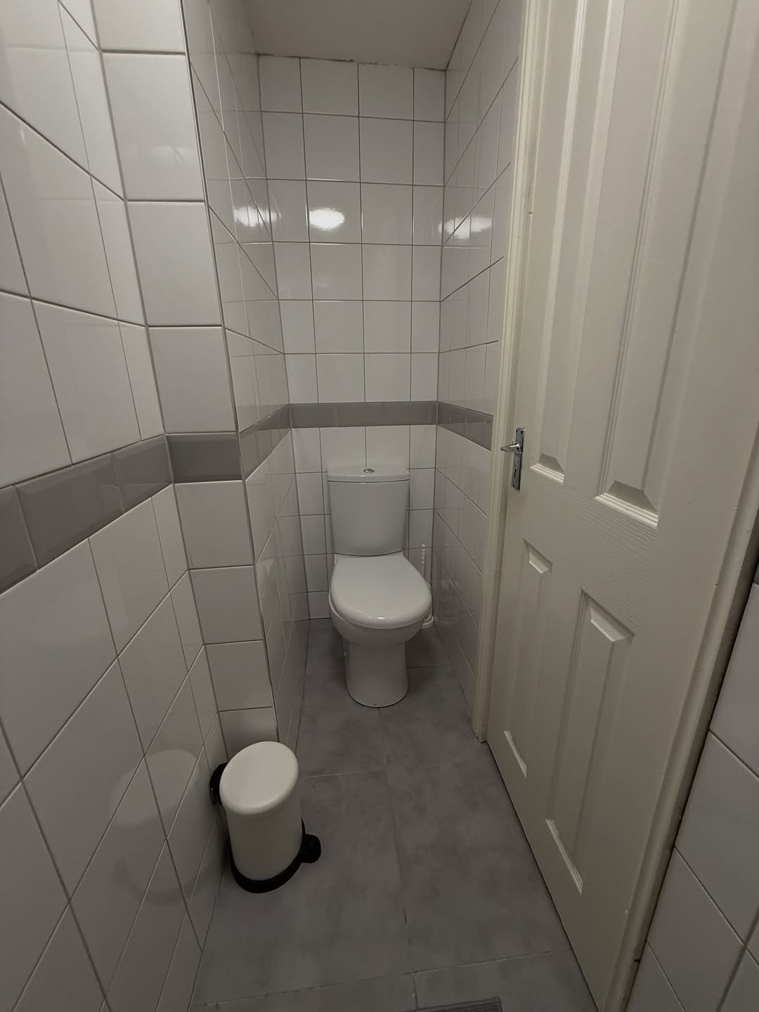 Small bathroom with white toilet, tiled walls, and gray trim.