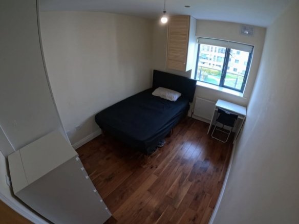 Small bedroom with bed, desk, window, and hardwood floor. Neutral colors.