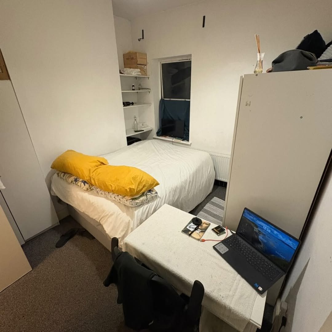 Small bedroom with bed, desk, laptop, and storage. Cozy, minimalist interior.