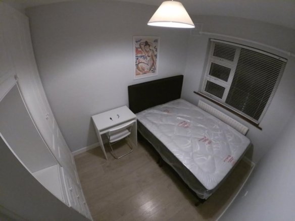 Cozy bedroom with bed, desk, wardrobe, and window. Natural light and simple decor create a comfortable space.