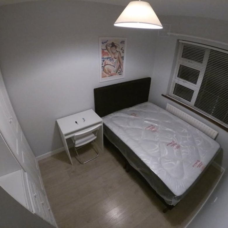 Cozy bedroom with bed, desk, wardrobe, and window. Natural light and simple decor create a comfortable space.