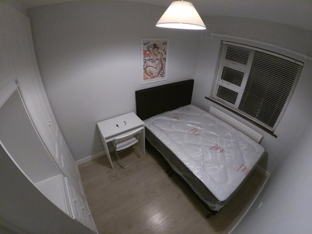 Cozy bedroom with bed, desk, wardrobe, and window. Natural light and simple decor create a comfortable space.