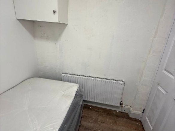 Small bedroom with bed, radiator, cabinet, and white walls. Minimalist interior design.