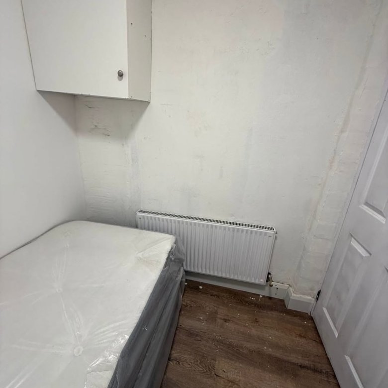 Small bedroom with bed, radiator, cabinet, and white walls. Minimalist interior design.