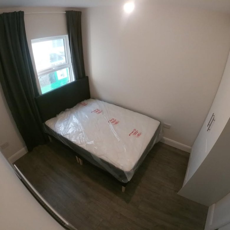 Small bedroom with bed, wardrobe, window, and dark green curtains.