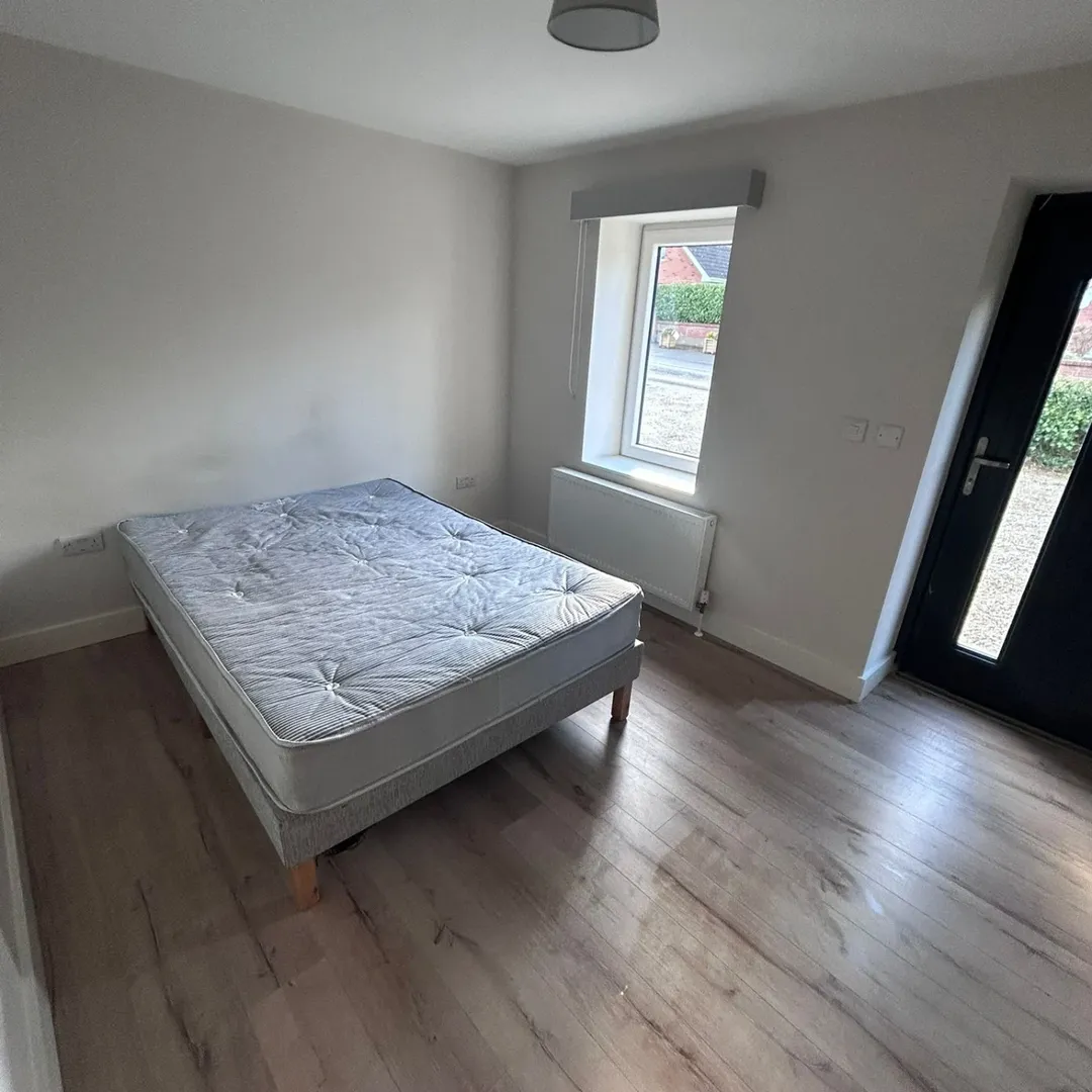 Small bedroom with bed, window, and wood flooring.
