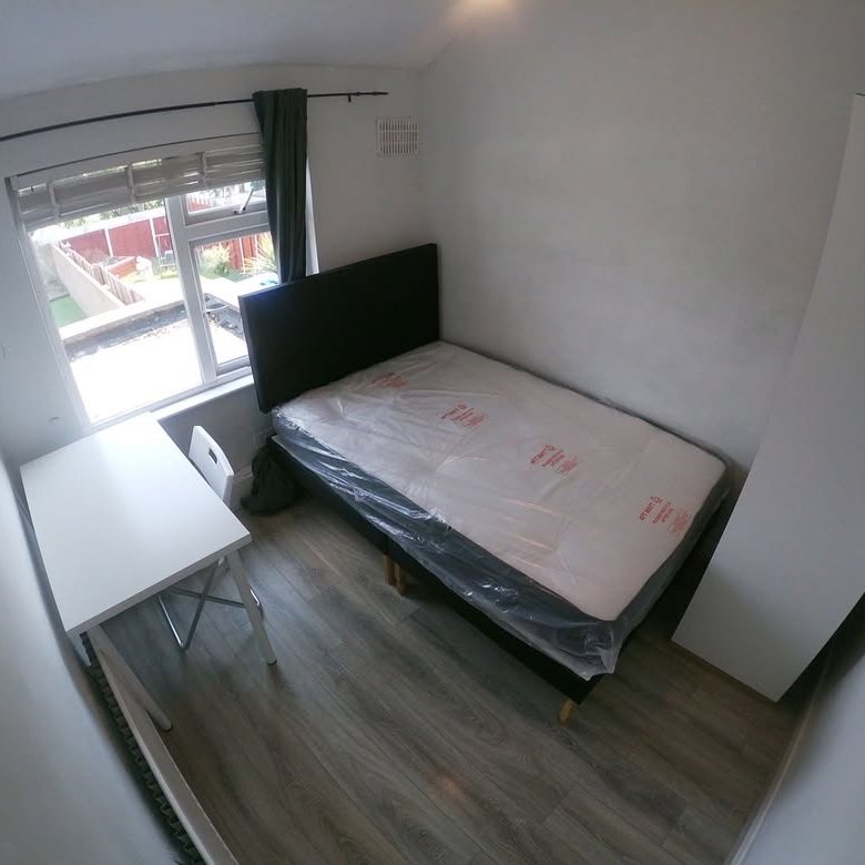 Small bedroom with single bed, desk, wardrobe, and window overlooking a garden.