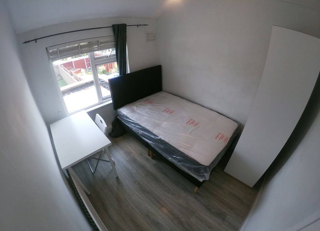 Small bedroom with single bed, desk, wardrobe, and window overlooking a garden.